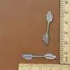 Silver leaf-shaped metal findings with ruler showing size for scale on brown background