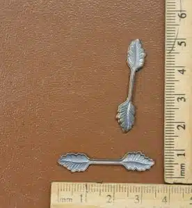 Silver leaf-shaped metal findings with ruler showing size for scale on brown background
