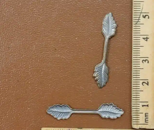 Silver leaf-shaped metal findings with ruler showing size for scale on brown background