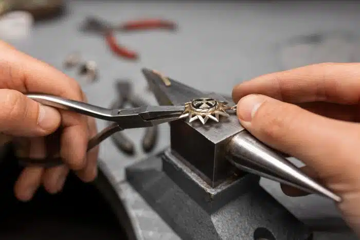 Jeweler uses pliers to shape a star-shaped metal pendant held in a bench vise.