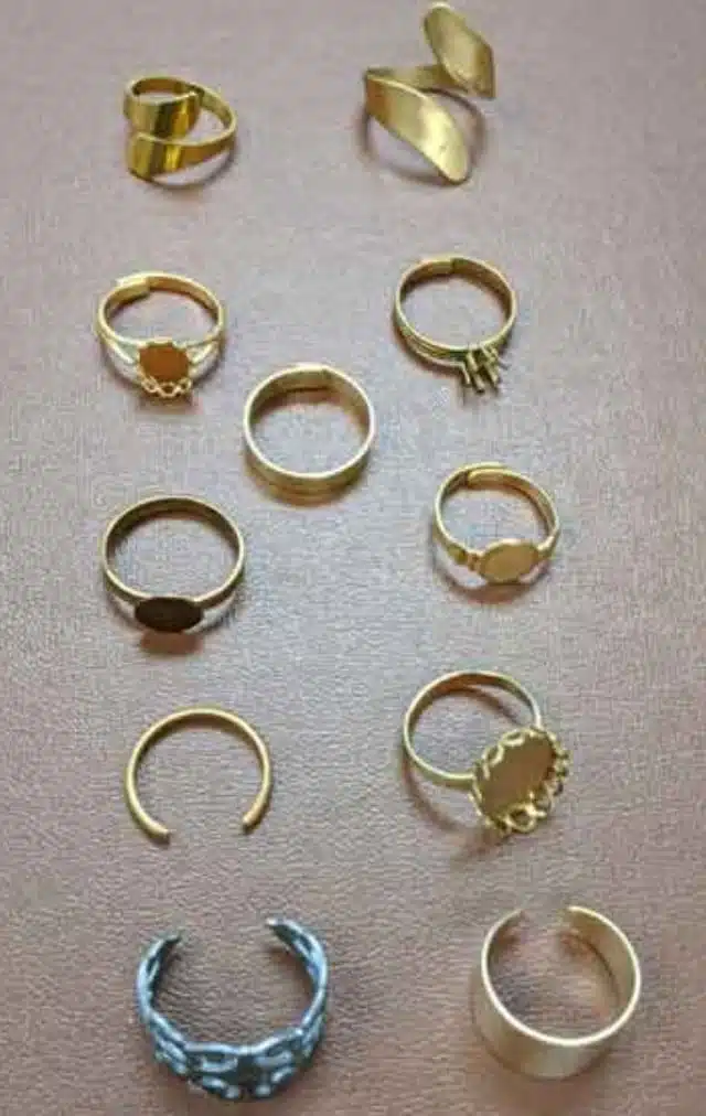 Collection of gold rings with various designs laid out on a light pink surface, showing different bands and settings.